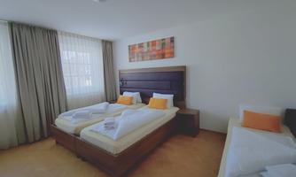 A bright room with two large beds and an additional bed. There are large windows with curtains and colorful cushions on the beds.