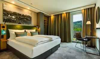 A modern hotel room with a comfortable double bed and a beautiful view of the landscape. The decor is stylish and well-lit.