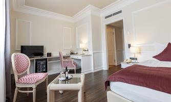 An elegant hotel room with a comfortable bed and stylish furniture. The room features a television and a desk in a bright, modern ambiance.