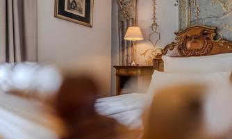 A cozy bedroom with an elegant bed and a decorative wall. A soft light from a lamp creates a warm atmosphere.