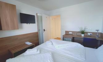 A bright room with two beds, a television, and a desk. The furniture is modern and the walls are in neutral colors.