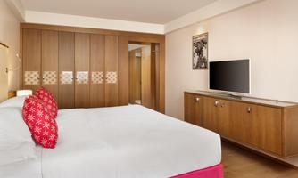 A modern hotel room with a large bed, a television, and wooden furniture. The walls are painted in neutral colors, giving the room a cozy atmosphere.