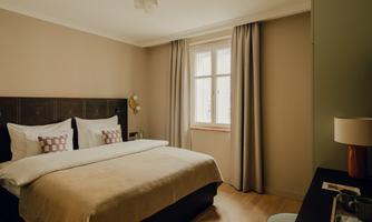 A modern bedroom with a large bed and soft pillows. The room has bright walls and curtains that create a cozy atmosphere.