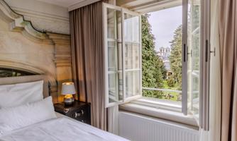 A cozy bedroom with an open window. Outside, a green landscape is visible.