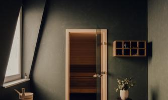 A modern bathroom with a clear, minimalist design. A glass door leads to the sauna, and a small flower sits on a table.