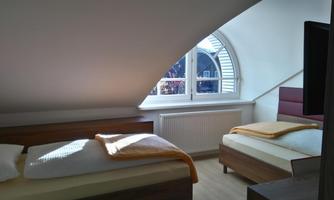 A cozy bedroom in the attic with two single beds and a large window. The furniture is modern, and there is daylight that brightens up the room.