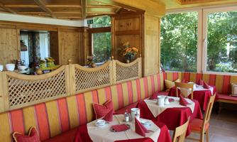 A cozy restaurant with wood paneling and red tables. Large windows let in plenty of light and offer a view of the greenery.