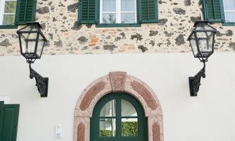 A historic building with an elegant entrance door. Stylish lanterns hang on the sides and the windows are adorned with green shutters.