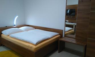 A modern bedroom with a double bed and bright bedding. Next to the bed is a small table and a wall mirror.