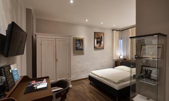 A modern bedroom with a double bed and wooden flooring. Pictures hang on the wall, and there is a desk as well as a TV.