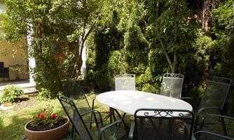 An inviting garden with a white table and several chairs. Surrounded by green trees and colorful flowers.