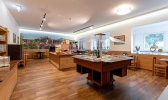 A modern restaurant with warm wooden flooring and an inviting buffet area. The walls are adorned with pictures, and large windows allow plenty of daylight in.