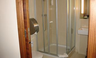 A modern bathroom with a shower, toilet, and a sink. The glass shower and the light walls create a clean ambiance.