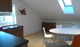 A modern kitchen with wooden cabinets and a large, round table. The room has plenty of natural light through the skylight.