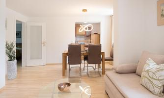 A bright and modern living room with a cozy sofa and a table. The room is simply and invitingly decorated.