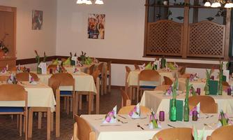 A cozy restaurant with several tables elegantly set. Flowers and decorative elements create an inviting atmosphere.