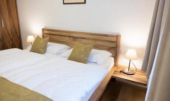 A cozy bedroom with a wooden bed and white bed linens. Next to the bed are two night lights and a wooden table.