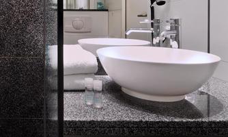 A modern bathtub made of white ceramic stands on an elegant dark granite surface. Towels and toiletries are neatly arranged.
