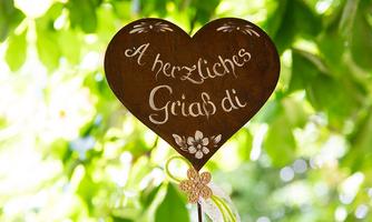 A heart-shaped wooden sign with the inscription "A heartfelt greetings to you". It is surrounded by green leaves.