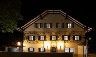 A historic building with a distinctive facade and bright windows at night. The architecture features traditional elements and inviting lighting.