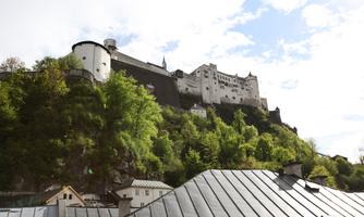 An impressive castle on a hill, surrounded by lush greenery. The blue sky and clouds provide a picturesque backdrop.