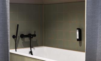 A modern bathroom with a white bathtub and a black faucet. The walls are tiled in soft green tones, and there are curtains that provide some privacy.