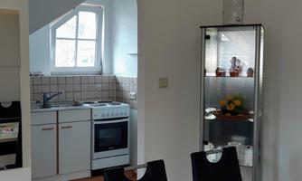 A bright kitchen with modern appliances and a dining area. Next to the kitchen is a glass table with decorative objects.