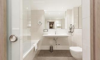A modern bathroom with bright tiles and a large mirror. There is a bathtub, a shower, and an elegant toilet.
