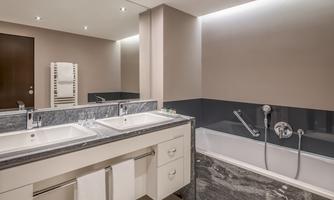 A modern bathroom with two sinks and a bathtub. The walls are in neutral colors, and there are stylish light fixtures.