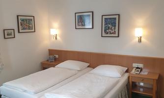 A cozy room with two single beds and warm light. Pictures hang on the walls, and a bedside table stands next to the beds.