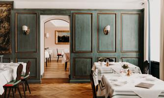An elegant restaurant with tastefully decorated tables and a stylish ambiance. The walls are painted in a soft green shade, creating a relaxed atmosphere.
