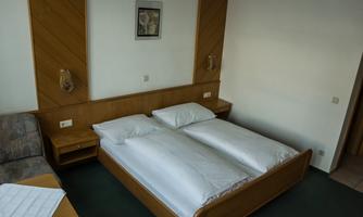 A cozy room with a double bed and a table. The walls are painted in light colors, and there is a comfortable seating area.