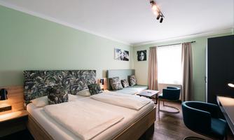 A modern hotel room with a double bed and a window that lets in plenty of light. The walls are painted in a soft green, and there are cozy seating areas.