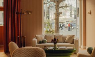 A cozy living space with a bright sofa and a green coffee table. Through the windows, you can see people walking outside.