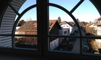 A view through a large window onto a quiet street with several houses. The sky is clear and it seems to be daytime.