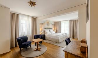 A stylish room with a large bed and cozy armchairs. The windows let in plenty of natural light and the floor is made of wood.