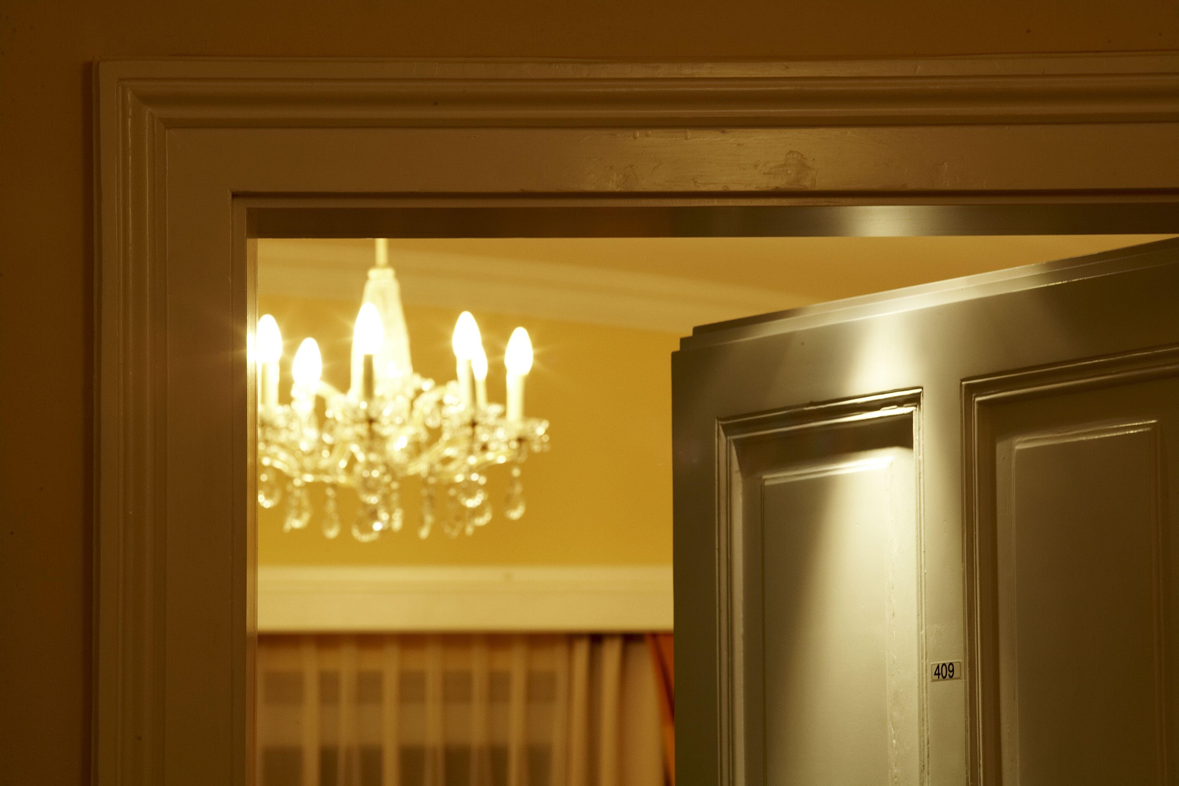 An open door with an elegant chandelier in the background. Soft light falls through the door frame.