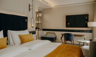 An elegant bedroom with a large bed and golden accents.  
On the wall, there is a television and there is a cozy armchair as well as a small table.