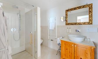 A modern bathroom with a shower, sink, and a large mirror. The wooden table gives the room a warm atmosphere.