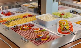 A lavish buffet featuring various types of sausages, cheese, and fresh vegetables. On top, there are also salads and dressings in bowls.