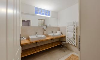 A modern bathroom with two sinks on a wooden shelf. The walls are bright and the room is well-lit.