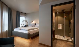 A modern hotel room with a large bed and a shower. The room is bright and friendly decorated.