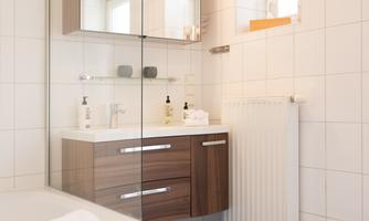A modern bathroom with a wooden washbasin and a large mirror. The walls are bright tiled, and there is plenty of natural light.