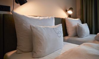 A cozy bedroom with several pillows on the beds. Soft lighting creates a relaxing atmosphere.