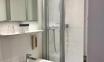 A modern bathroom with a shower and a sink. The walls are kept in bright white, providing an inviting atmosphere.