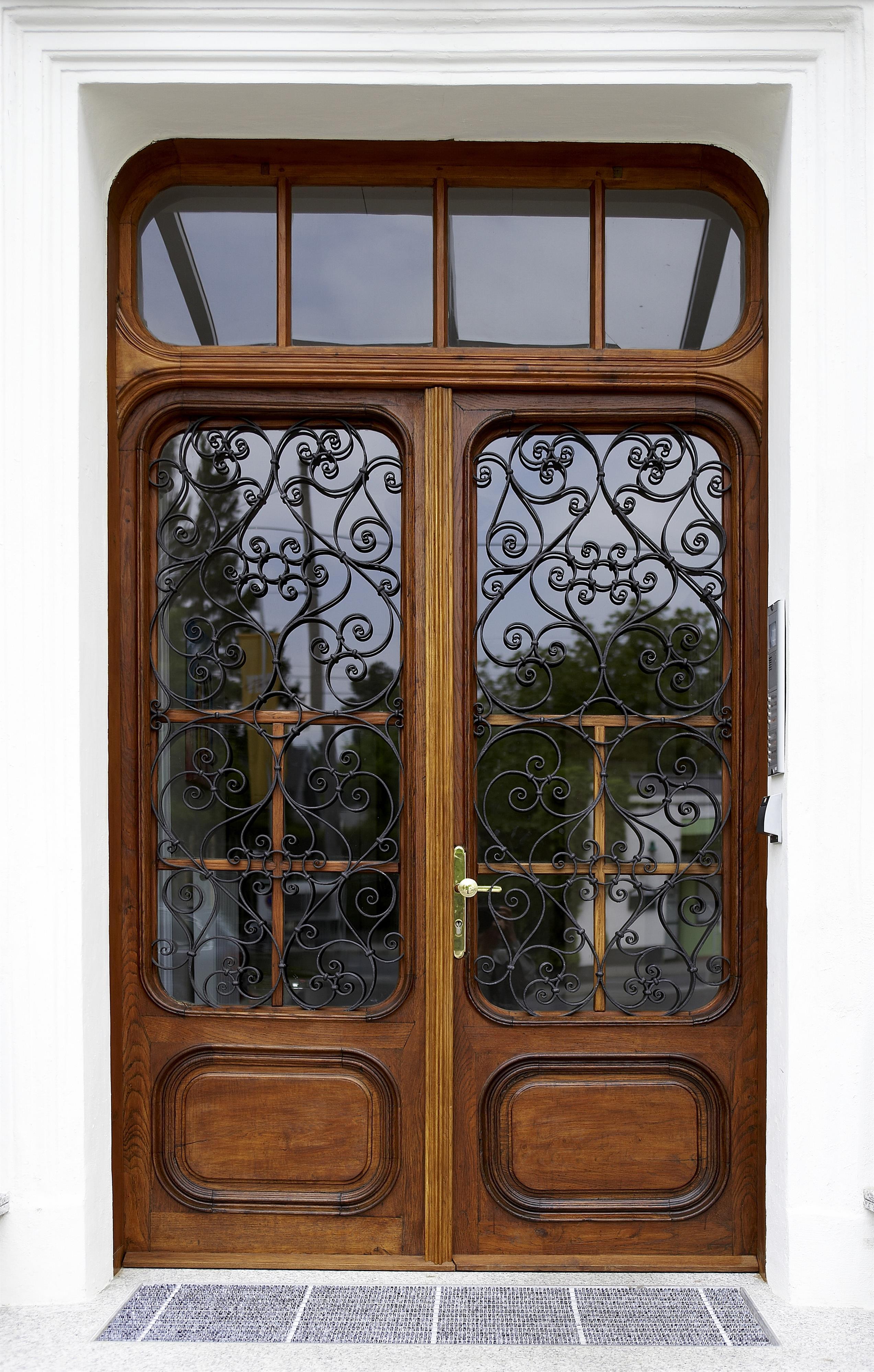 An elegant wooden door with ornate wrought iron in the windows. The door is set in a bright, modern frame.