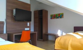 A modern hotel room with a television, a desk, and a wardrobe. The walls are painted in neutral tones, and there is a type of colorful wall art.
