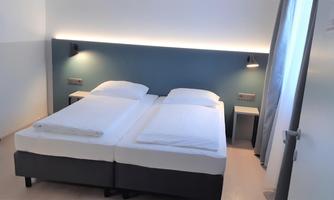 A modern bedroom with two single beds and soft lighting. The walls are in a subtle color tone, creating a relaxed atmosphere.