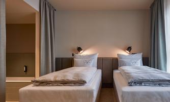 A cozy room with two single beds and modern amenities. The walls are light, and the curtains create a pleasant atmosphere.