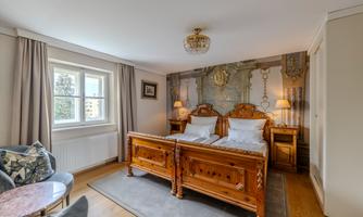 A stylish bedroom with two cozy beds and elegant furniture. The walls are artistically decorated and the room is well lit.